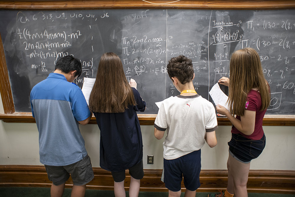 Four CTY students working on math problems at a chalkboard