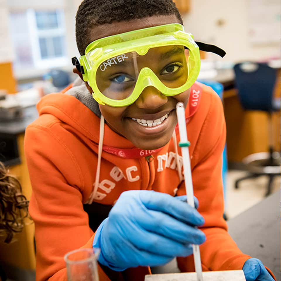 CTY student Raaka M. doing a science experiment, wearing goggles