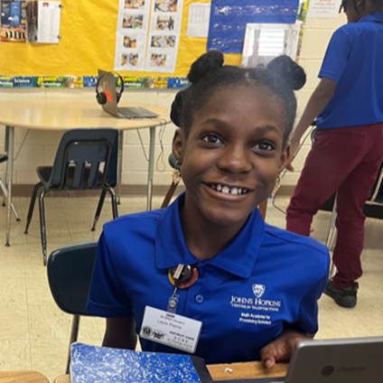 CTY student wearing a blue polo shirt and sitting at a desk in a classroom.