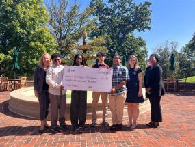 Several Johns Hopkins Center for Talented Youth members standing in front of a fountain and holding a donation check from AT&T.