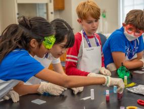 Four young CTY students all wearing aprons and two wearing lab goggles