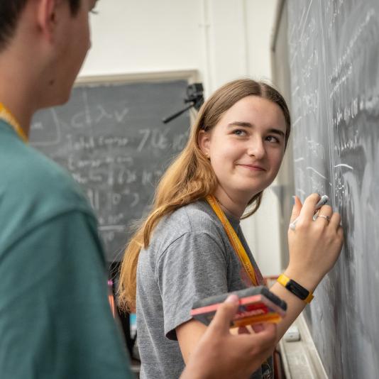 Two bright students writing on a chalkboard during a CTY in-person course