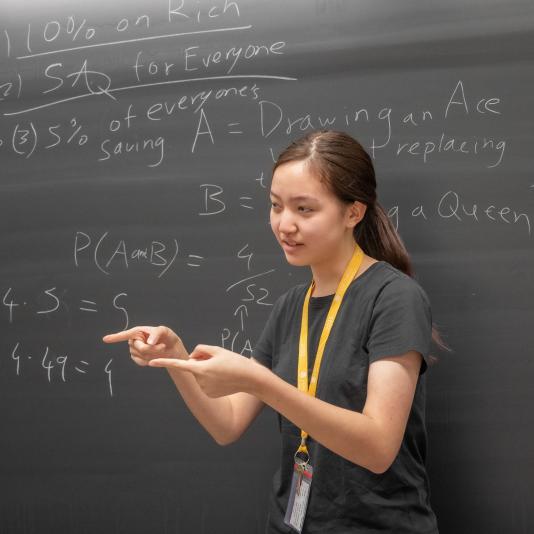 a CTY student standing in front of a chalk board that has math equations writtenon it.