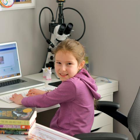 Young CTY Online student at desk with laptop and microscope