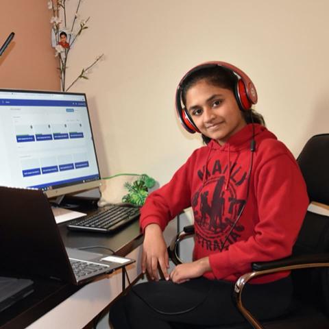 CTY Online Programs student sitting desk with 2 open computers, wearing headphones