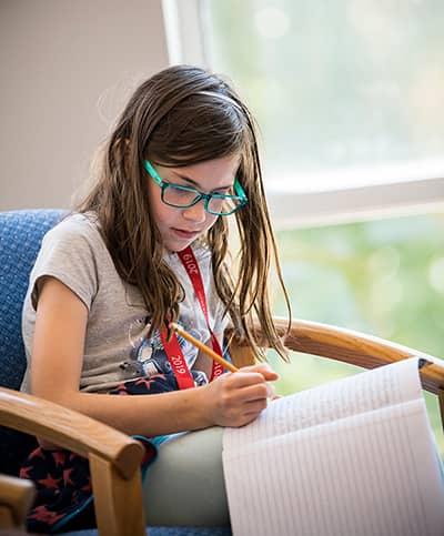 Student sitting in a chair writing in a notebook.