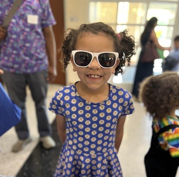 Girl smiling and wearing sunglasses and a dress with the Pi symbol on it.