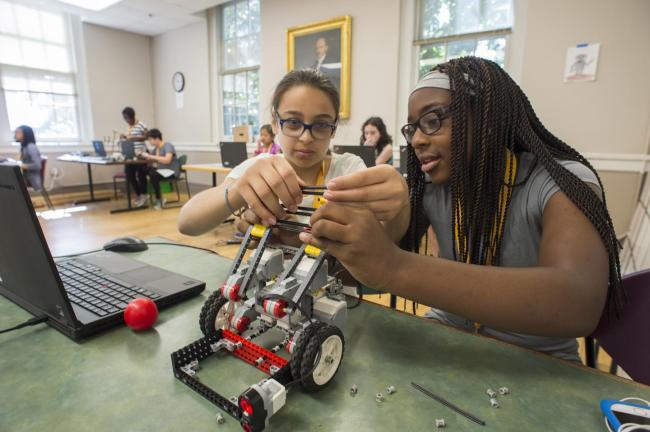 Two students build a car together out of Lego-like bricks