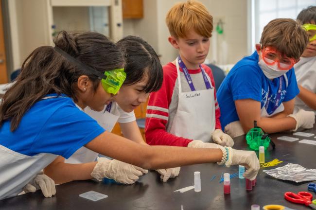 Four young CTY students all wearing aprons and two wearing lab goggles