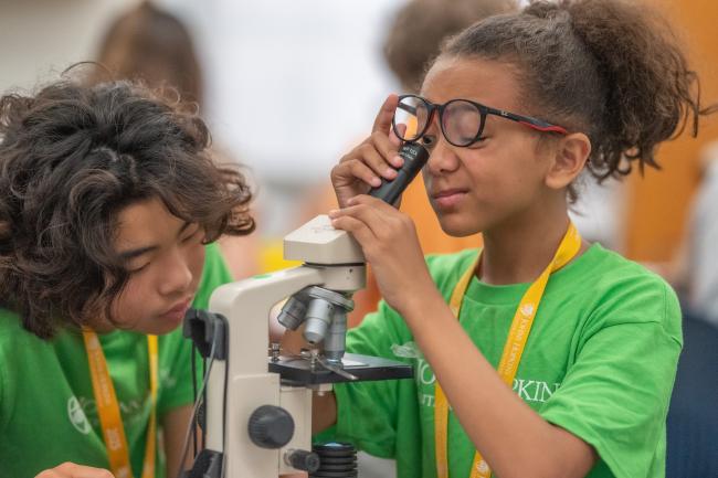 Two young CTY advanced learners wearing green shirts and working with a microscope